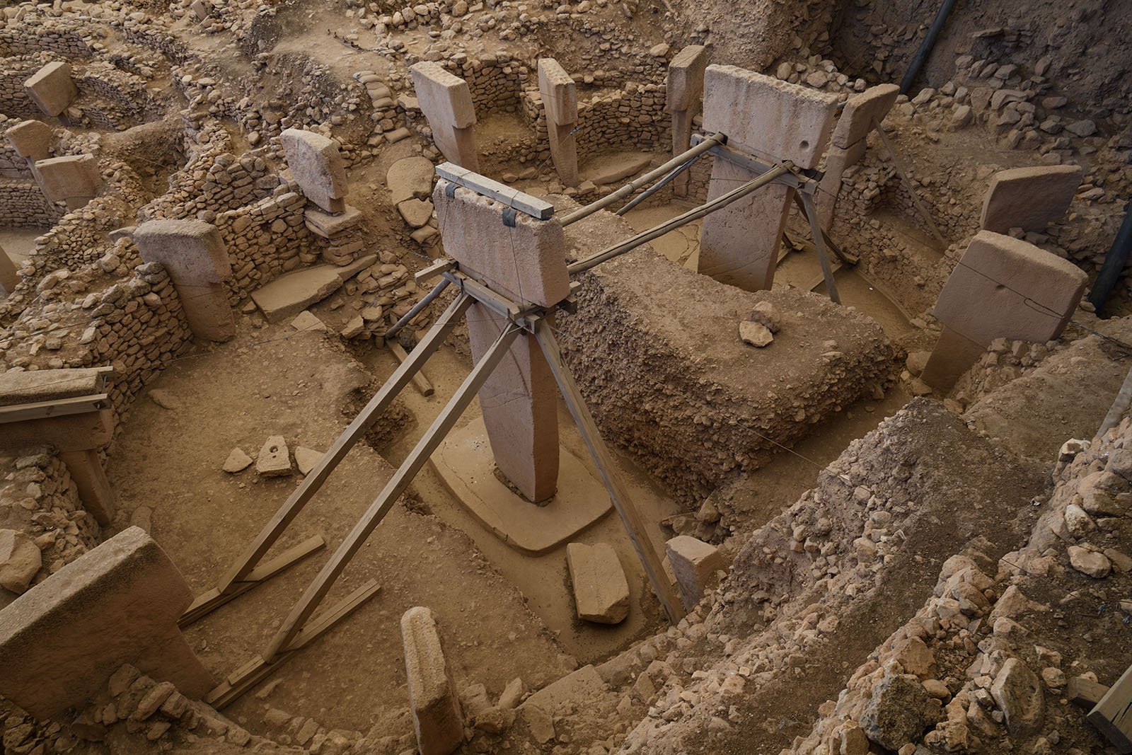 An excavated round stone building with a ring of pillars and two tall T-shaped pillars in the middle, held up by wooden supports